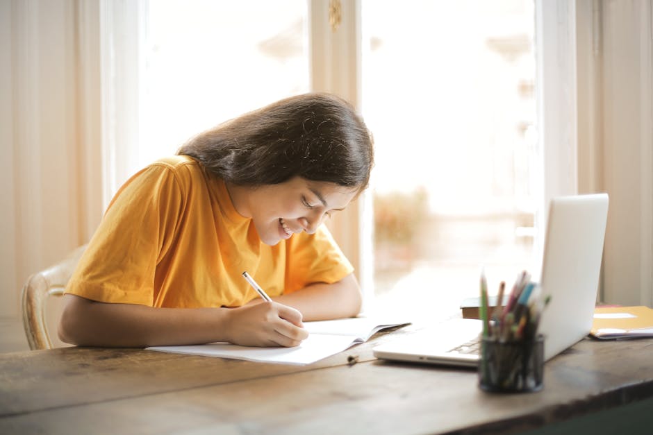 Young woman studying with a laptop and notepad at home, smiling and focused