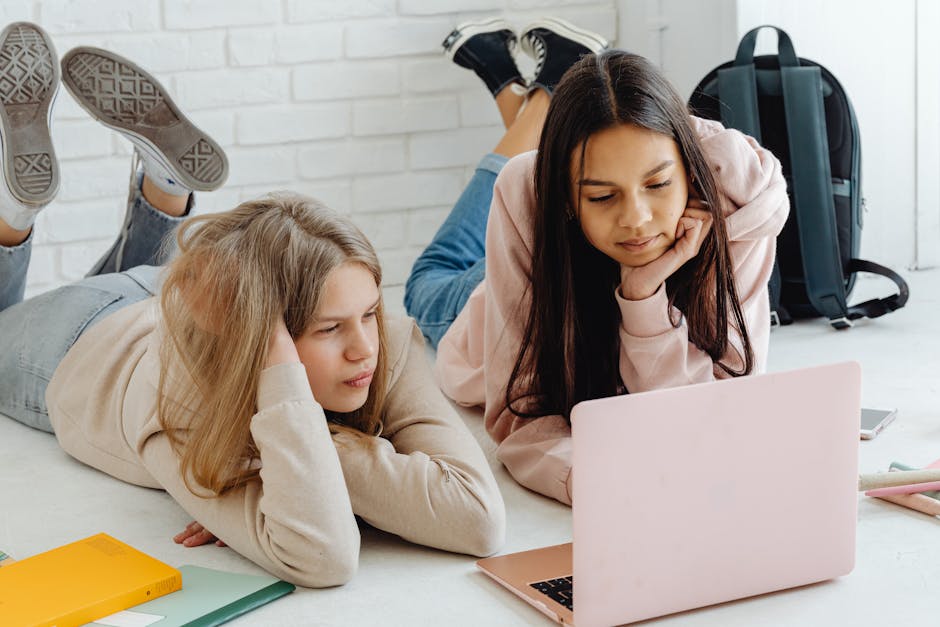 Two teenage girls studying together using a laptop indoors, emphasizing friendship and education