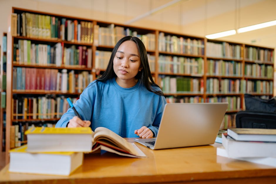 Young woman studying in a library with books and laptop, focusing on education