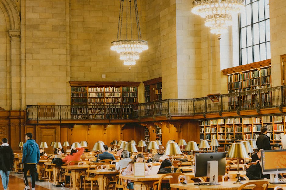 Spacious and elegant library interior with chandeliers and people studying at wooden tables.